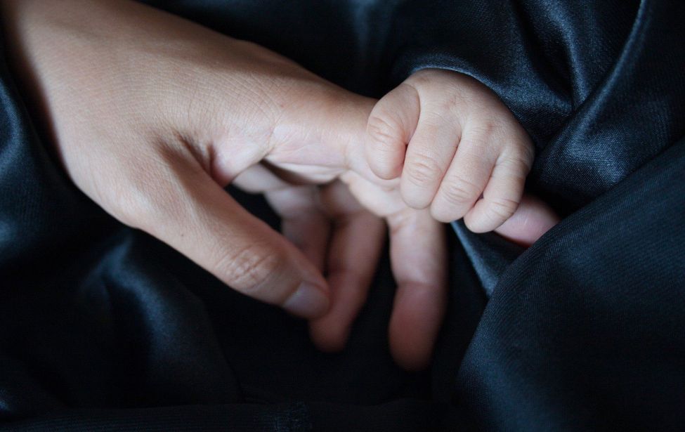 Fotografie einer Babyhand, die den Finger eines Erwachsenen hält