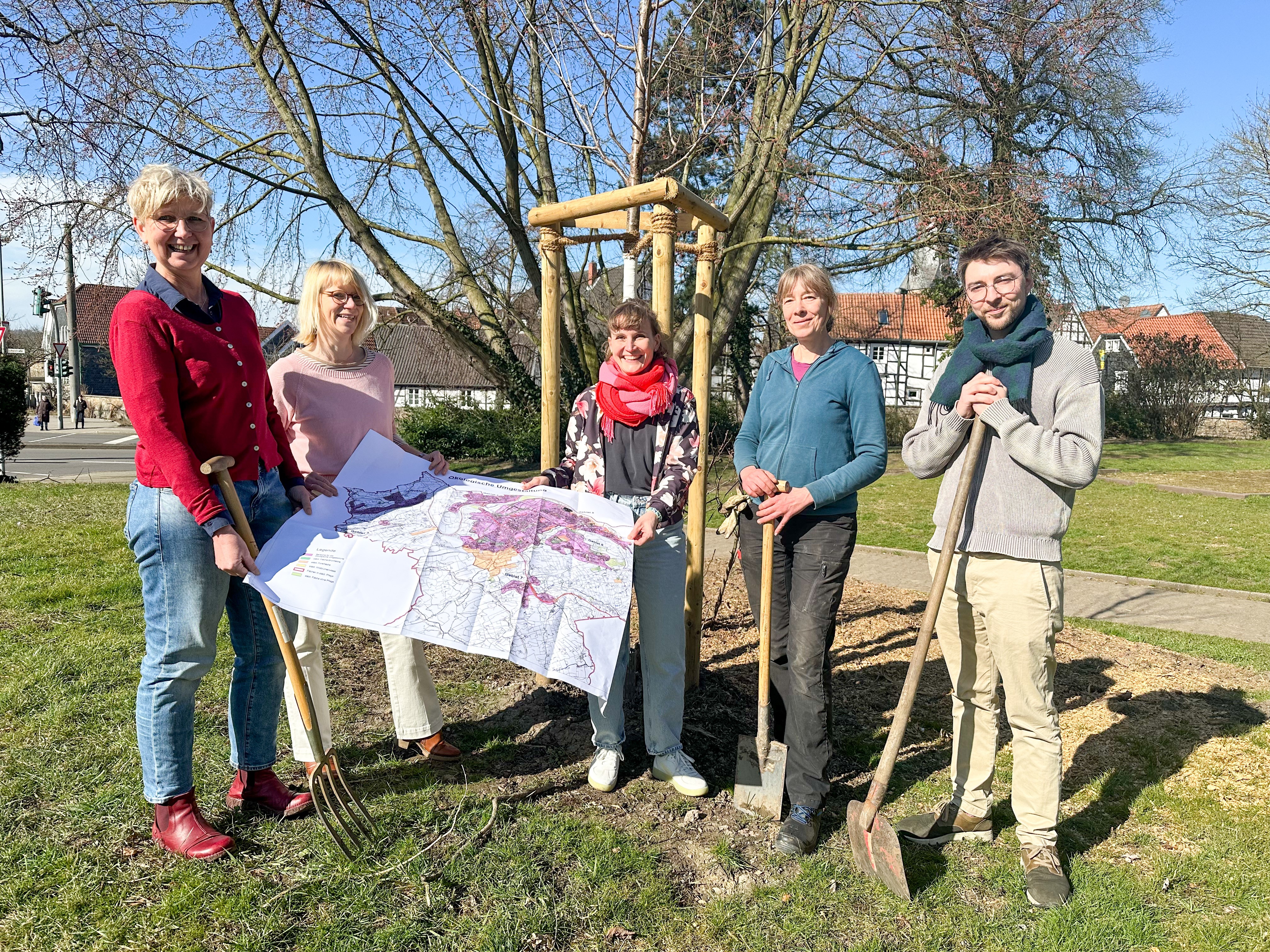 Ingenieurinnen mit Plan und Gartengerät vor neuem Baum im Park