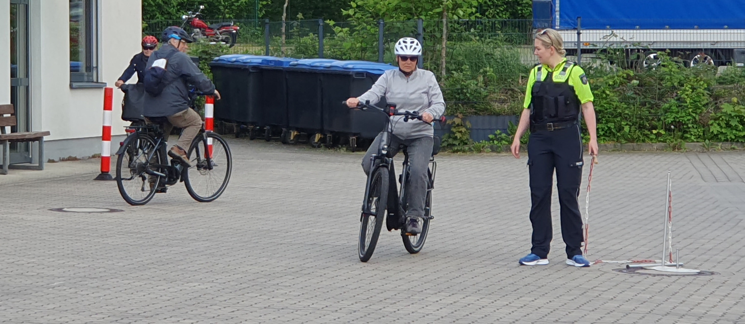 Eine polizistin übt mit drei Seniorinnen und Senioren an einem Parcour sicheres Radfahren