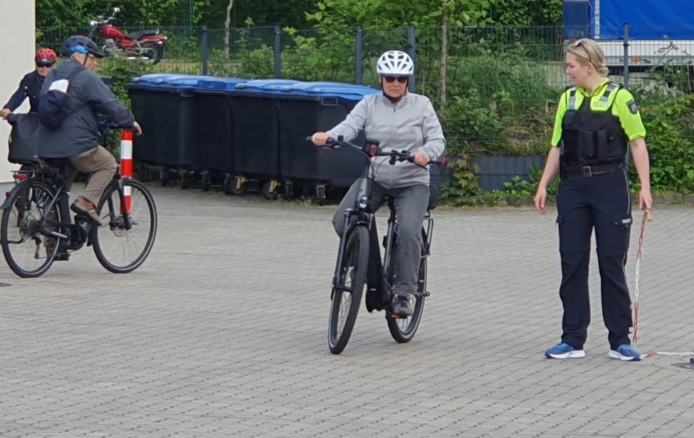 Eine polizistin übt mit drei Seniorinnen und Senioren an einem Parcour sicheres Radfahren